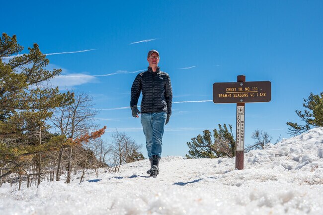 A man walks along the Sandia Crest trail on top of the snowy Sandia mountains.