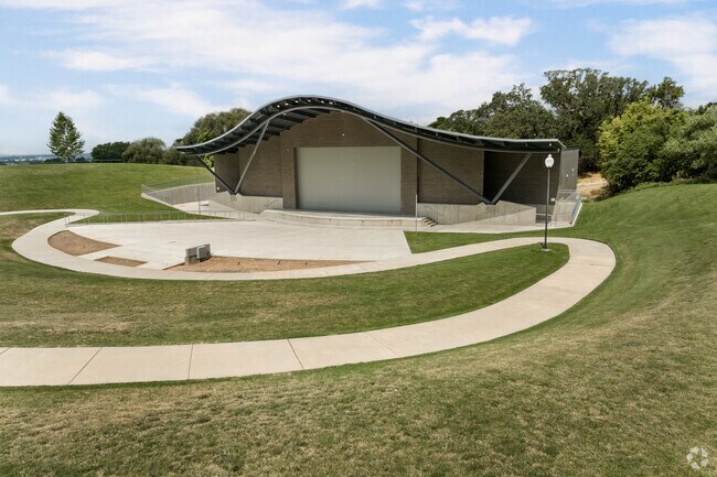 Barker Park has an amphitheater with a curved roof surrounded by grass and cement trails.