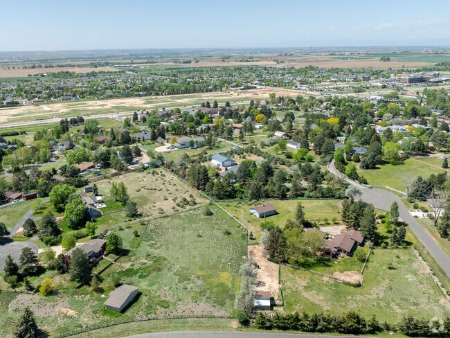 An aerial view of Westridge in Greeley, CO, reveals a picturesque blend of spacious homes, expansive green spaces, and serene natural features like lakes and grazing cattle, offering a tranquil, semi-rural atmosphere.