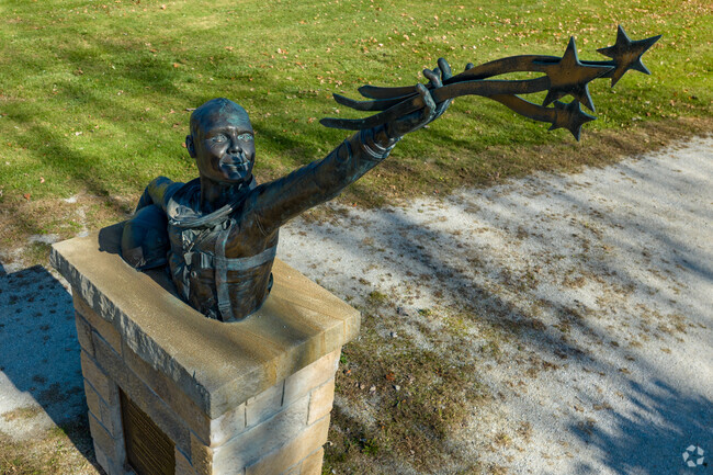The statue of John Glenn is reaching skyward toward stars with vapor trails at John Glenn Grove.