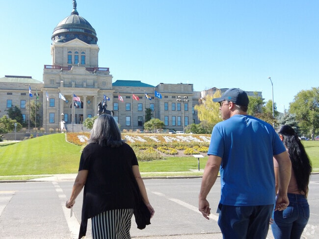 The Montana State Capitol is surrounded by trees and green grass, ideal for a walk.