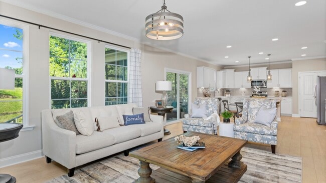 Family room with large windows and kitchen with white cabinets, pendant lights, and glass double door in Angier, NC.