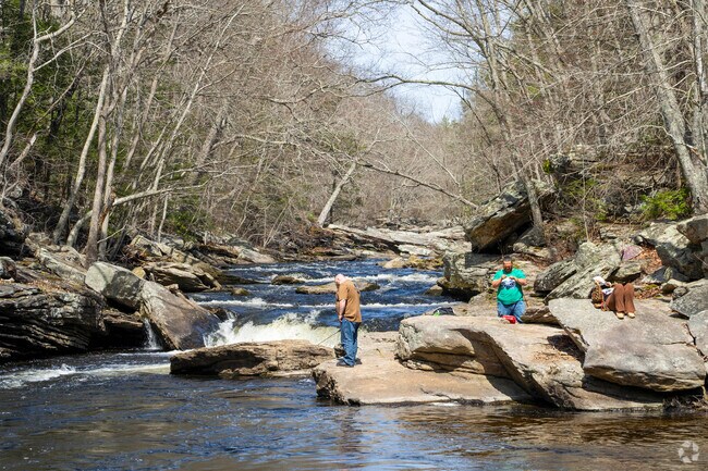 A man fishes while a person reads a book in the sun on the rocks of the Shetucket River in Scotland.