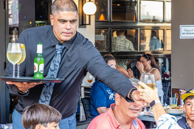 A server moves gracefully between tables, balancing a tray lined with glistening glasses at the Hub in Bexley, FL.