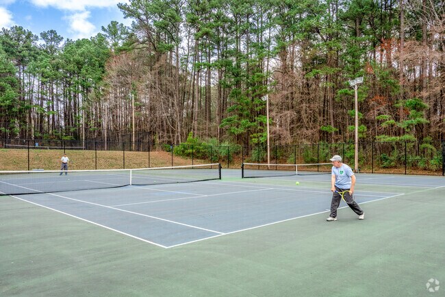 Residents enjoy a friendly game of tennis at Rock Quarry Park, a beloved green space in Durham’s Walltown neighborhood, surrounded by tall pines and tranquil nature.