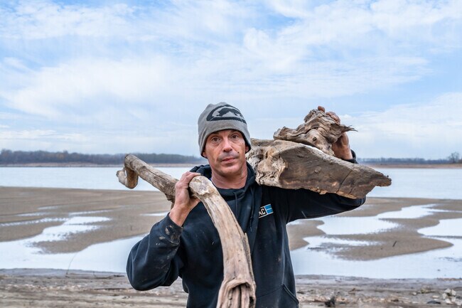 A man hoists driftwood onto his shoulders at North Riverfront Park near Glasgow Village.
