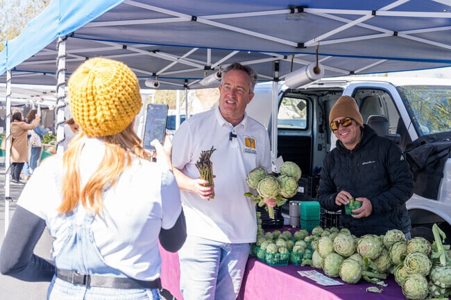 A man promotes asparagus and artichokes at the Newhall Farmer's Market in Newhall.