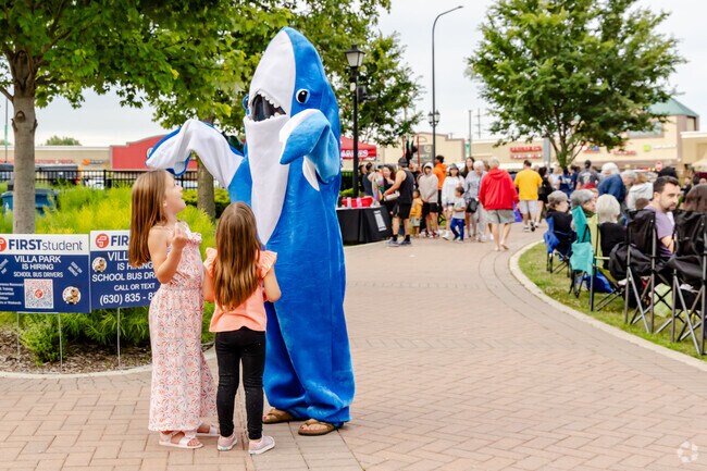 Children dance joyfully with a shark at Rock 'N Wheels event.