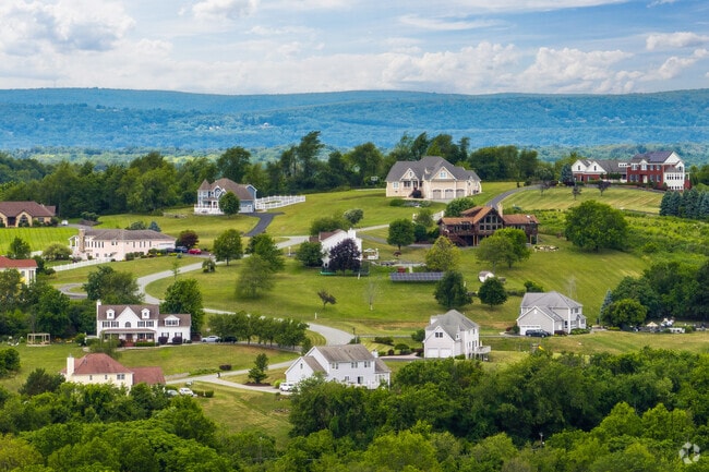 Picturesque hillside neighborhood in the Wallkill Town, featuring elegant homes, winding driveways, and lush greenery against a backdrop of rolling mountains.