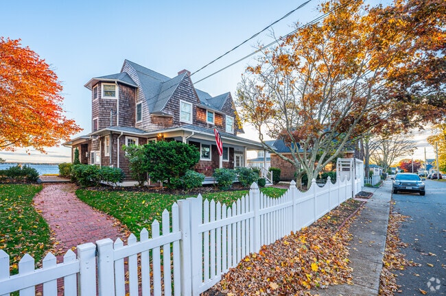 This large Cape Cod home in Conimicut-Shawomet features a white picket fence and a spacious front yard.