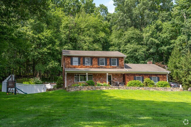 A Colonial Revival home with a porch and play area sits on a wooded lot in Southeast, New York.