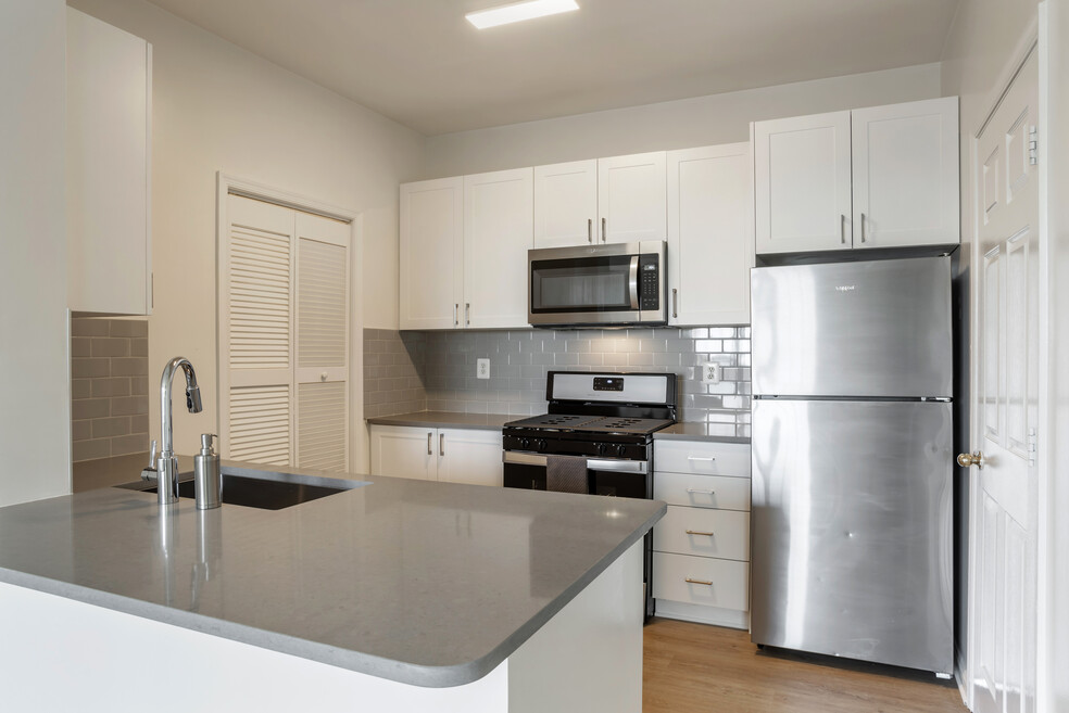 Renovated Package II kitchen with white cabinetry, grey quartz countertops, tile backsplash, stainless steel appliances, and hard surface flooring