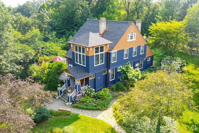 A Victorian-style home in Oconomowoc Lake featuring a colorful exterior, manicured gardens, and serene wooded surroundings.