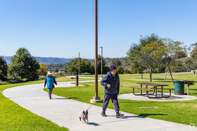 A winding sidewalk surrounds a grassy field with picnic tables and bbq's at Shadow Oak park.