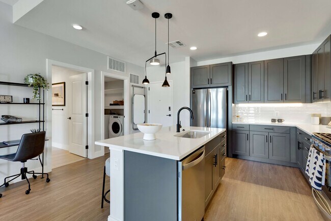 Modern kitchen with sleek dark cabinets, elegant pendant lighting, and a spacious island with integrated sink, offering a stylish workspace.
