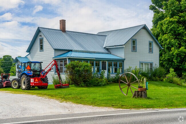 A farmhouse in Saint George has farm equipment on the lawn and a blue aluminum roof.