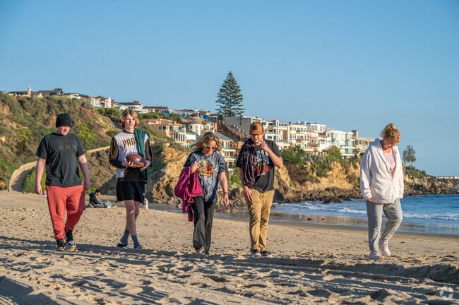 Strolling along Corona Del Mar State Beach, just outside Broadmoor Sea View, people enjoy the serene sands and stunning ocean views in Newport Beach's coastal paradise.