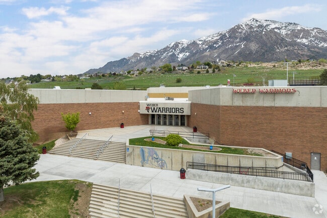 Weber High School in the foreground with green fields and snow capped mountains in the background in Pleasant View.
