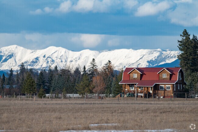 Glacier National Park cuts through the horizon above an Evergreen farmhouse and ranch land.