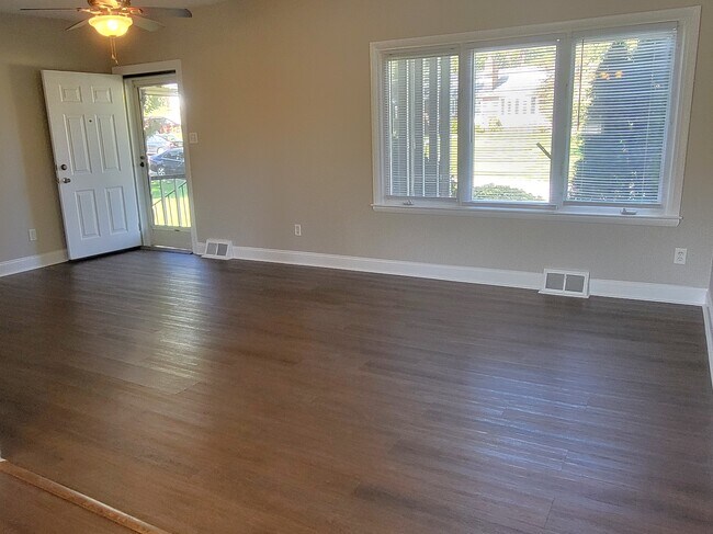 Living room with ceiling fan, large window, front door to screened in porch