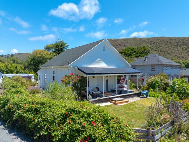 This white cottage features a broad front porch and is surrounded by native coastal plants.