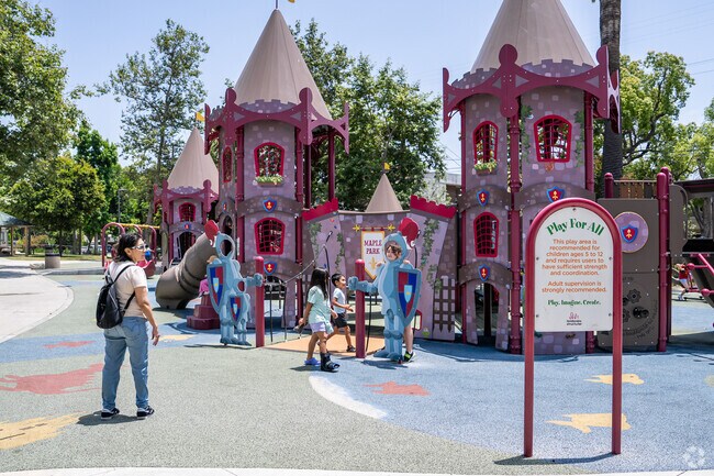 Children laugh and climb on the castle-themed inclusive playground, exploring tunnels, slides, and ramps designed for ages 2–12.