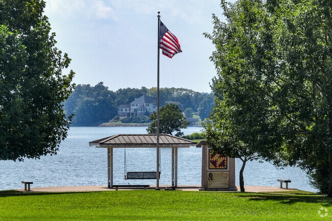 Carl Cowan Park in Concord offers lakeside seating beneath trees and a waving American flag.