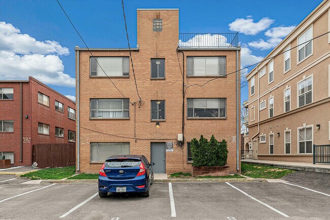 Charming brick apartment building with spacious parking area, set against a vibrant blue sky backdrop.