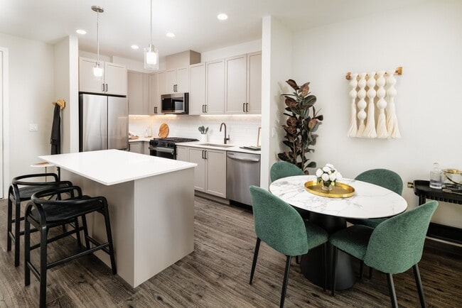 Kitchen and dining area with grey cabinetry, white quartz countertops, white tile backsplash, stainless steel appliances, and pendant lighting
