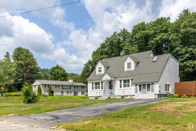 A group of homes, including a Cape Cod-style house, sits on an open lot in Hill, New Hampshire.