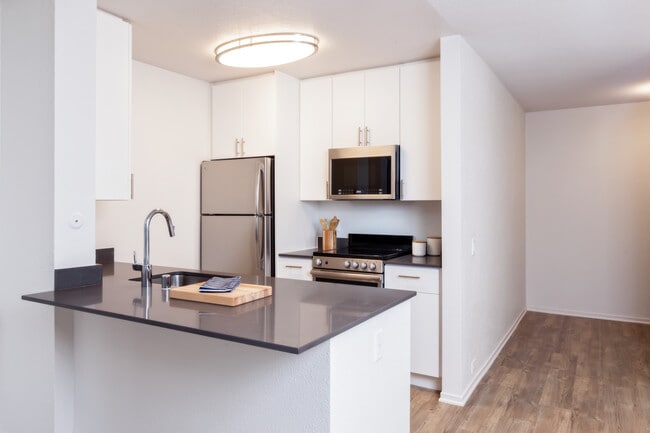 Renovated Package I kitchen with stainless steel appliances, dark grey quartz countertops, white cabinetry, and hard surface flooring