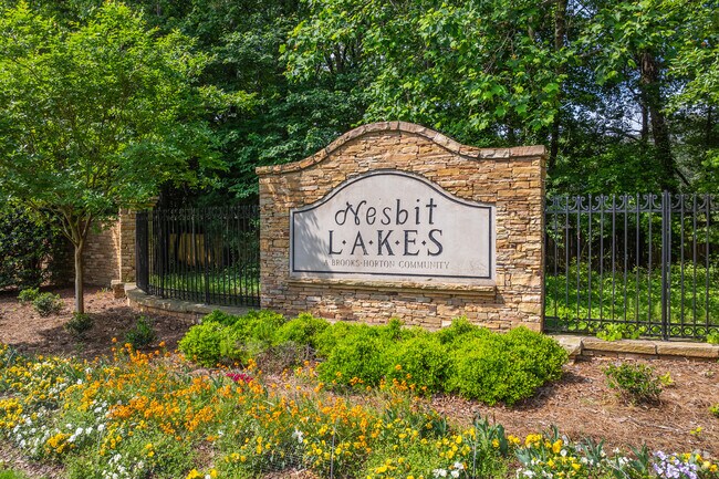 A stunningly landscaped stone monument, adorned with intricate carvings and vibrant floral arrangements, majestically marks the entrance to the picturesque Nesbit Lakes neighborhood, welcoming residents and visitors alike with its timeless beauty and charm.