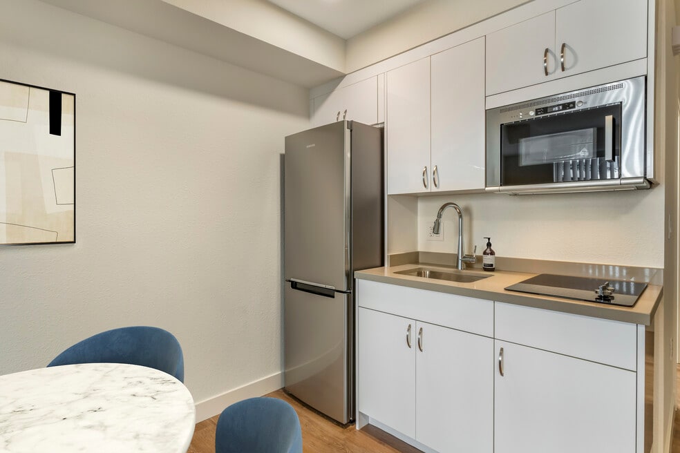 Renovated Package II kitchen with stainless steel appliances, beige quartz countertops, white cabinetry, and hard surface flooring