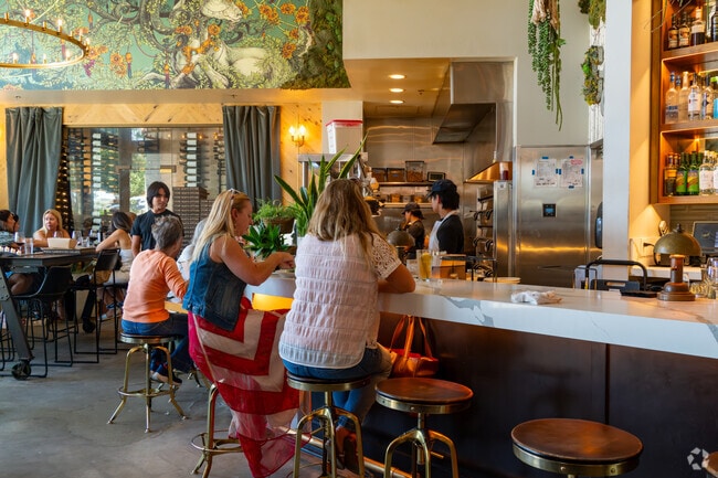 Stylish interior of The Goat & Vine restaurant with guests dining at a modern bar under hanging greenery.