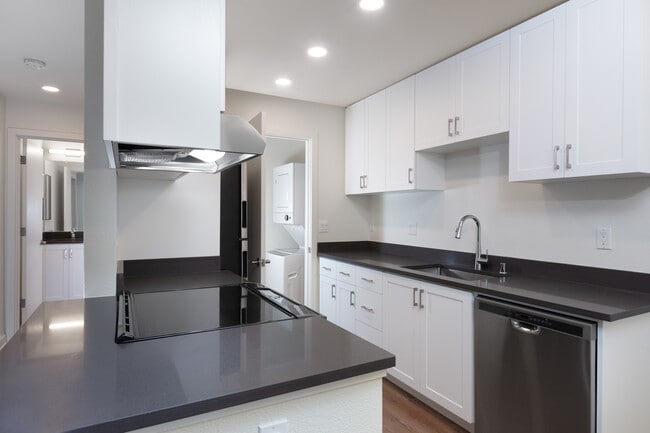 Kitchen with white cabinetry, stainless steel appliances, dark grey countertops and hard surface flooring