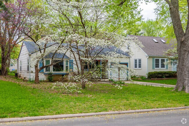 An updated bungalow home is obscured by a small blooming Dogwood tree.