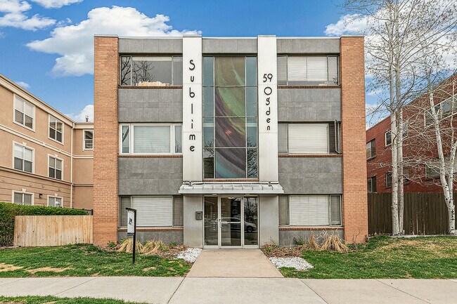 Modern apartment exterior of Sublime 59, showcasing chic architecture with contrasting brick and concrete facade under a vibrant blue sky.