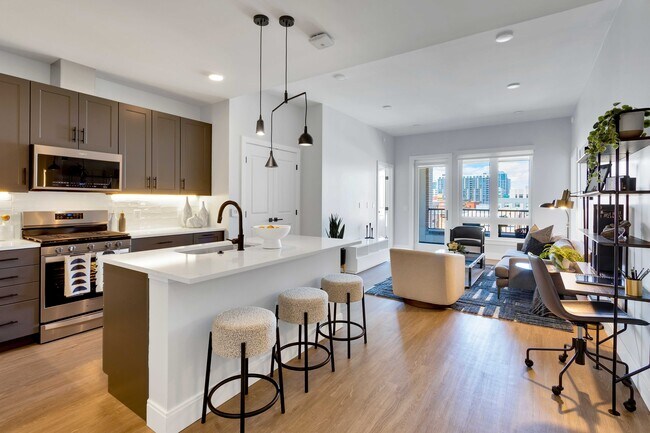 Modern open-plan kitchen and living area with sleek cabinetry, a chic island with bar stools, and large windows offering vibrant city views.