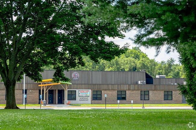 Northeast Elementary School is set back from the road behind lush trees.