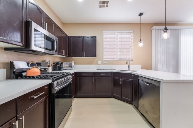 Kitchen featuring stainless steel appliances, a peninsula, dark brown cabinets, hanging light fixtur