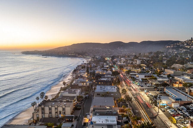 During the twilight hours, the Pacific Coast Highway near The Village comes alive with golden light, as the sun sets over the ocean, casting a warm glow on the road, cliffs, and coastal scenery.
