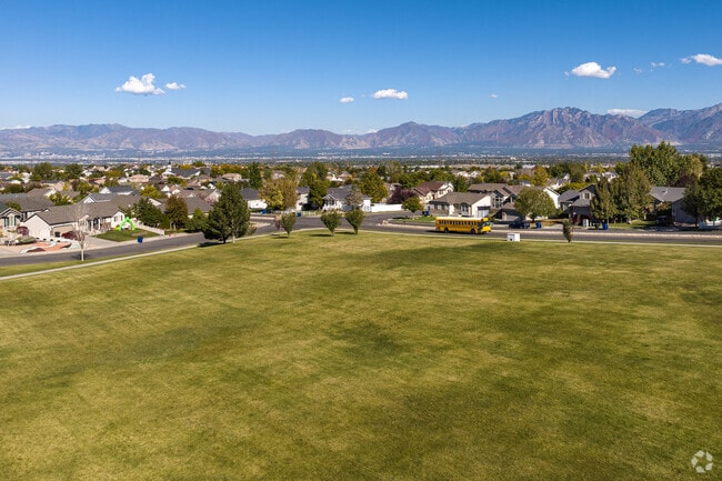A picturesque scene of a yellow school bus in front of the lawns at Oquirrh Highlands Park.