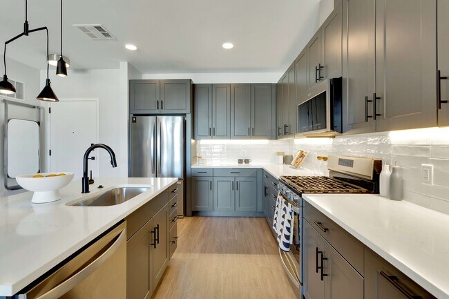 Modern kitchen with sleek grey cabinets, stainless steel appliances, and elegant pendant lighting, offering a bright and inviting atmosphere.