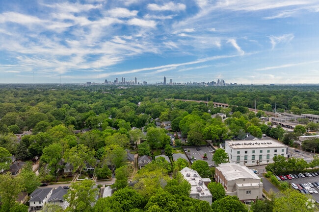 The vibrant Oakhurst neighborhood is surrounded by lush greenery with the iconic Atlanta skyline rising in the distance, highlighting its perfect balance of residential charm and urban proximity.