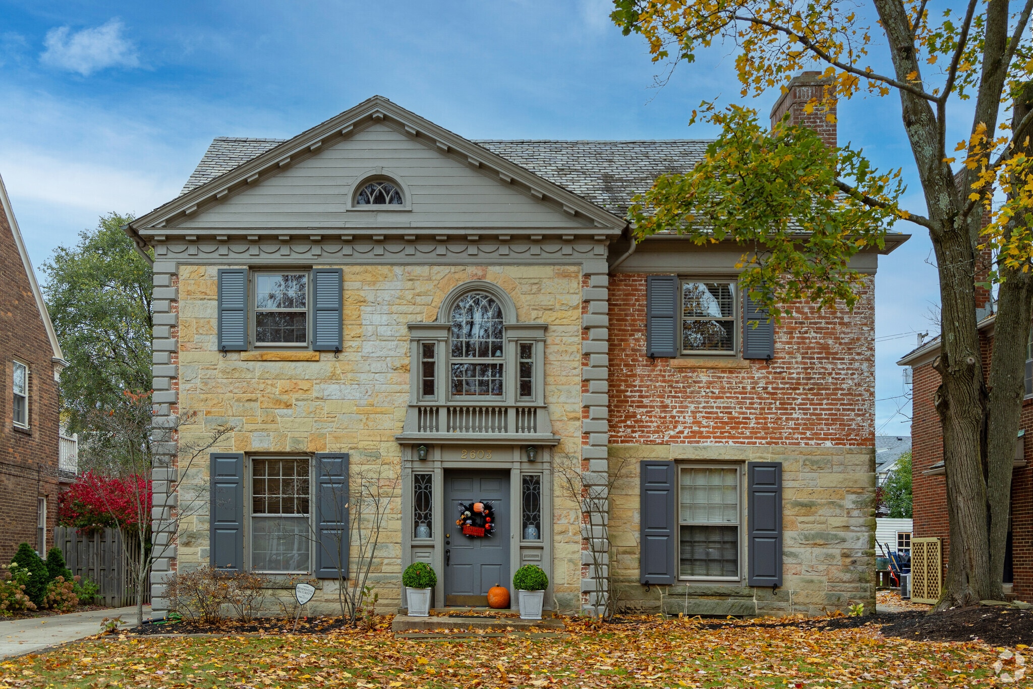 A multi color brick colonial blanketed with brightly colored fall leaves in University Heights.
