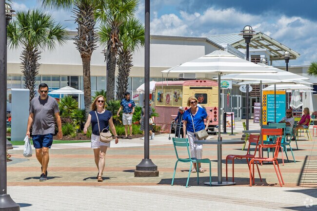 Shoppers explore sunny walkways and boutiques near Grande Dunes at Tanger Outlets.
