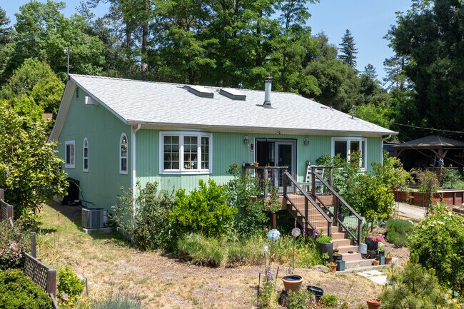 This Cottage-style home in Ben Lomond features arched windows, green siding, and a vibrant garden entry.