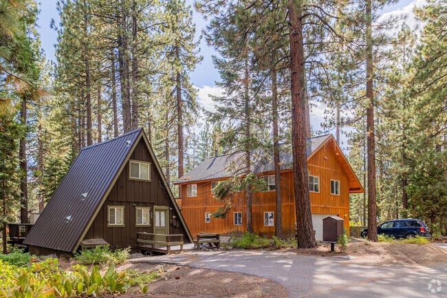 A small a-frame sits beside a larger wood mountain home.
