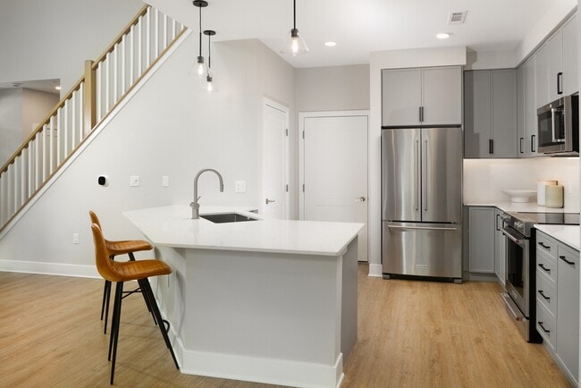 Signature Collection Townhome kitchen with upgraded stainless steel appliances, white quartz countertops and backsplash, grey cabinetry, hard surface flooring, and pendant lighting.