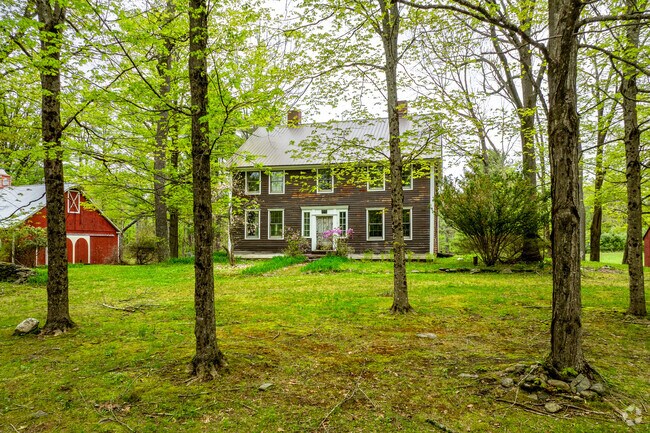 A colonial revival style home with weathered clapboard siding in Plainfield sits beneath the trees for added privacy.